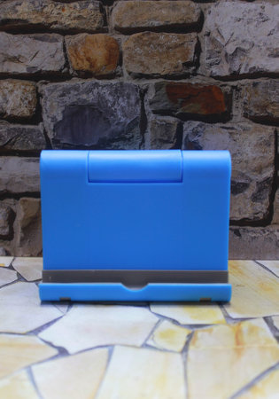 Photo of a blue plastic cell phone holder with a stone wall as a background on a stone motif tableの写真素材
