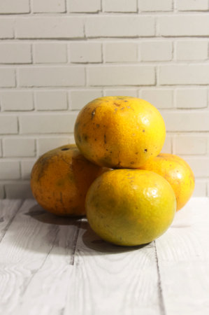Photo of four sweet oranges on a wooden table with a stone wall backgroundの写真素材