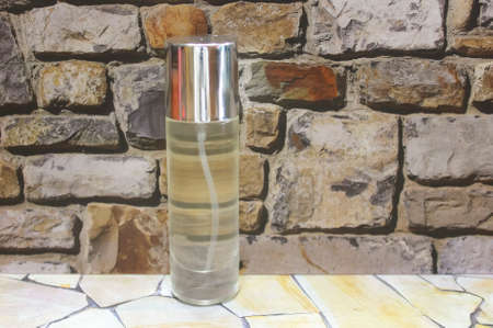 Photo of a refillable Perfume bottle on a wooden patterned table against a stone wall backgroundの写真素材