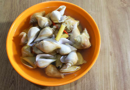 Photo of Batam's Indonesian seafood menu Snail GONG GONG boiled in an orange bowl on a wooden tableの写真素材