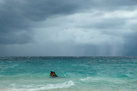 Moalboal. Cebu. Philippines - 06 aug 2016: Philippine young couple swimming in stormy tropical sea under cloudy dramatic sky of coming storm between big waves at gray dayのeditorial素材