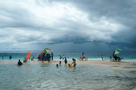 Moalboal. Cebu. Philippines - 06 aug 2016: Philippine families getting fun and rest while storm is coming to the tropical beach, from wavy sea under cloudy grey skyのeditorial素材