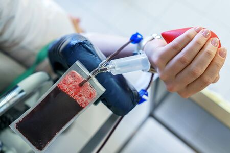 young caucasian woman with toy heart in the hand donates blood for saving lives and medical research in some hospital at day timeの写真素材
