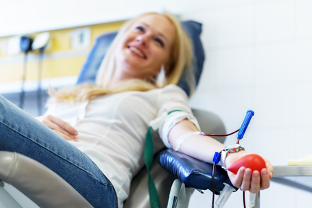 young caucasian woman with toy heart in the hand donates blood for saving lives and medical research in some hospital at day timeの写真素材