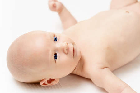 caucasian infant baby with beautiful blue eyes is lying on white surfase at day time