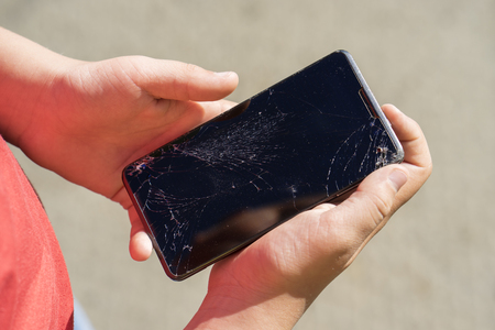 teen is holding some black phone with broken screen after falling down