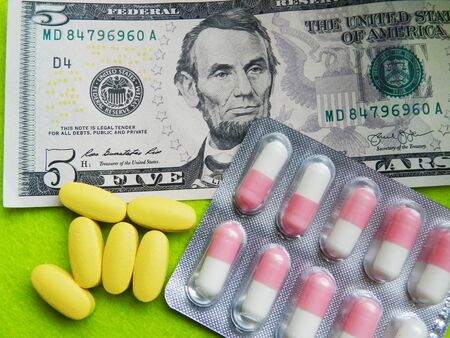 Close up photo with five dollar banknote and yellow pills on the green background