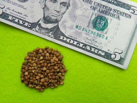 Buckwheat grain on the five dollar banknote on the green background illustrated the high prices of...