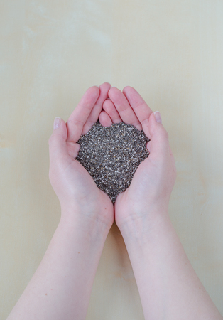 Chia seeds in female hands on a background of wooden tableの写真素材