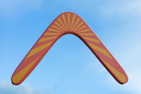 Wooden australian boomerang in flight against of pure white clouds and blue sky.の写真素材