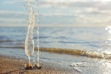 A tall glass with splashes of wine on the seashore. Sunsetの写真素材