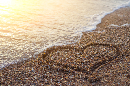 Heart on a sand of beach with wave on backgroundの写真素材
