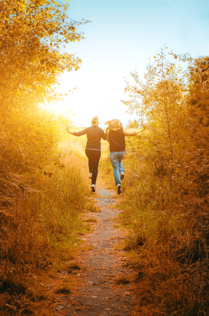 Two happy girls run away into sunset field backgroundの写真素材