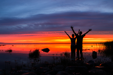 Two happy husband and wife with their hands up at a fiery sunset.の写真素材
