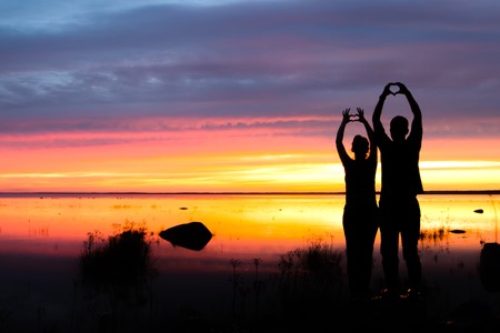 Two happy husband and wife with their hands up at a fiery sunsetの写真素材