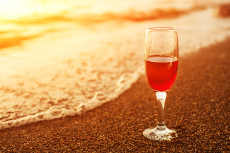 Romantic beach scene: glass of red wine at sunset near water lineの写真素材