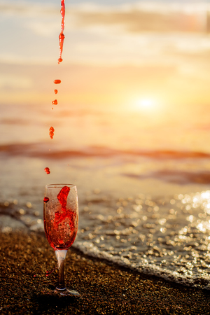 Romantic beach scene: glass of red wine at sunset near water line with splashesの写真素材