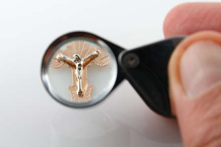 Jeweler with magnifying glass examine gold cross with Jesusの写真素材
