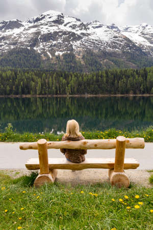 enjoying nature, girl sitting on a bench near the lake and looks on big mountainsの写真素材