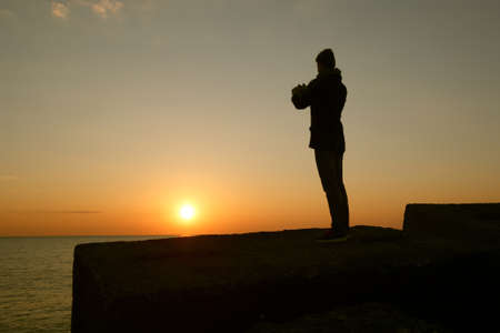 A man taking a photo of the sunset with his phoneの写真素材