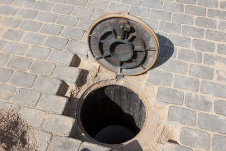 An open sewer hole in a brick paved roadの写真素材