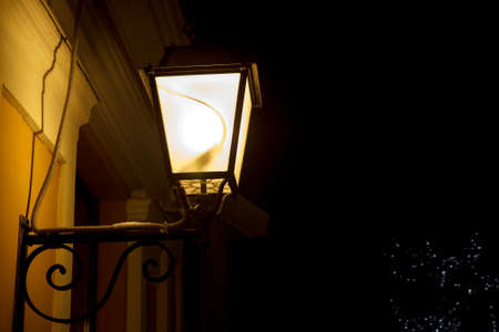 A lit light post holding by a wall on dark background