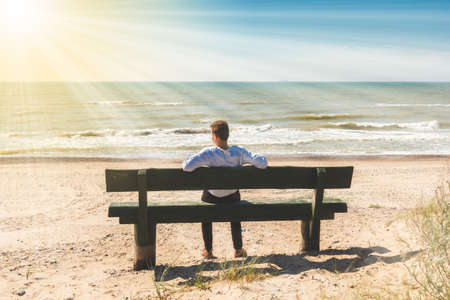 young man sitting on a bench near sea