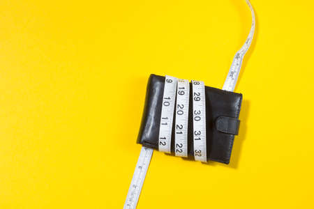 concept of budget and money. Purse is tied with measuring tape on yellow background