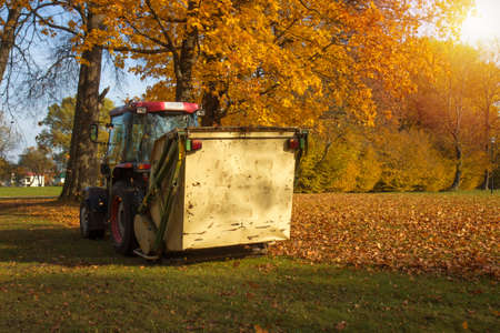 Vacuum sweeper towed by a tractor work in autumn park. Collect leafs.