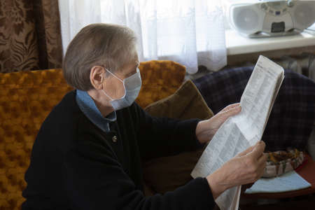 Senior woman reading newspaper, sitting in her sofa in her living roomの写真素材