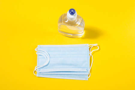Alcohol gel hand sanitizer and disposable hygienic mask on yellow backgroundの写真素材