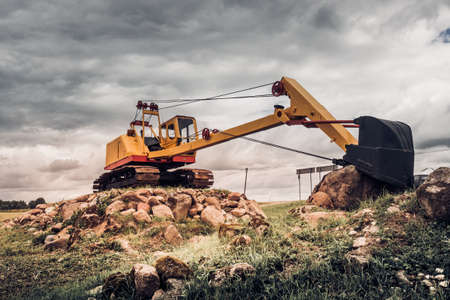 Excavator parked on stone ground against dark skyの写真素材