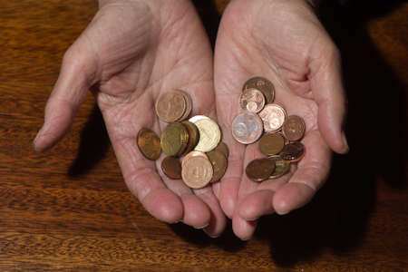 Wrinkled hands of elderly woman holding coins. Close up.