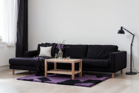 Dark purple sofa with a blanket beside a small table with bottles standing on black and white checkerboard floor in a minimalistic living room interior. Copy space. Real photoの素材