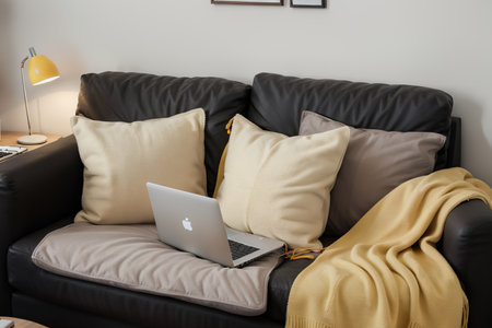 Laptop on gray sofa with yellow pillows and wool blanket on it. Blogger freelancer home workspace office. Modern colourful interior design concept.の素材