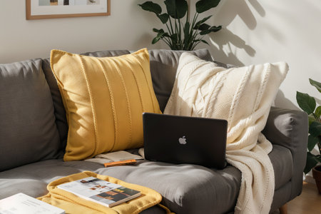 Laptop on gray sofa with yellow pillows and wool blanket on it. Blogger freelancer home workspace office. Modern colourful interior design concept.の素材
