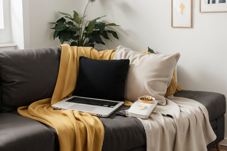 Laptop on gray sofa with yellow pillows and wool blanket on it. Blogger freelancer home workspace office. Modern colourful interior design concept.の素材