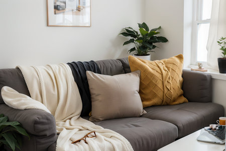 Laptop on gray sofa with yellow pillows and wool blanket on it. Blogger freelancer home workspace office. Modern colourful interior design concept.の素材
