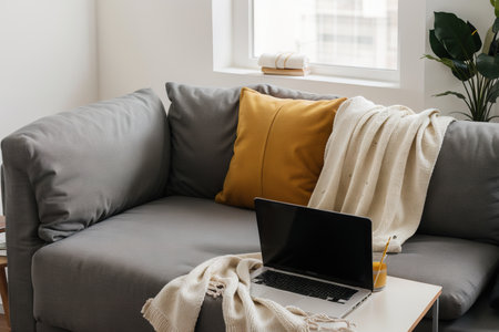 Laptop on gray sofa with yellow pillows and wool blanket on it. Blogger freelancer home workspace office. Modern colourful interior design concept.の素材