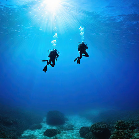 two Scuba divers Two scuba divers in silhouette swimming to the surface in the raysの素材