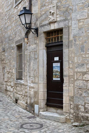 Les Baux-de-Provence, France - October 21, 2017. The entrance of an old stone town house with an antique wooden door, an iron lantern and a Pieta sculpture above the door. Stone pavement in front of the houseのeditorial素材