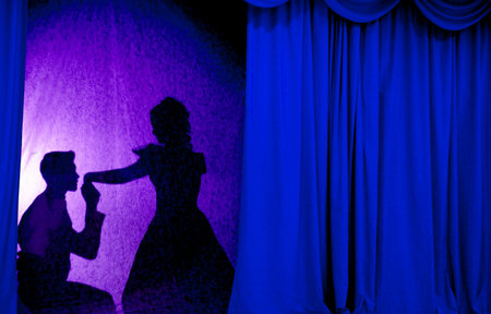 A man and woman in theatrical costumes in the theater of shadows on the stage with red curtains. Love in the shadows theater. Red curtain of opera, cinema or theater stage drapes.の写真素材