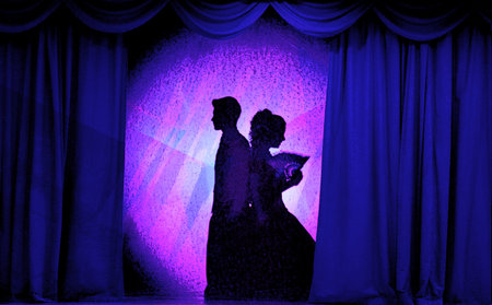 A man and woman in theatrical costumes in the theater of shadows on the stage with red curtains....