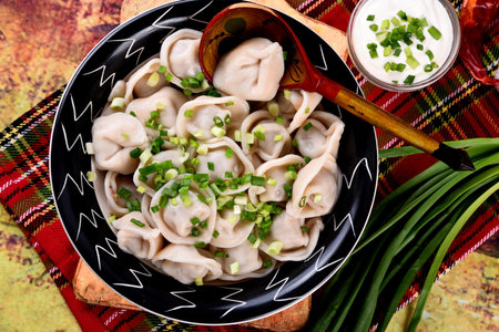 Cooked Meat dumplings (russian pelmeni) with green onion and sour cream on a plate, vintage...