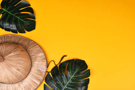 Reed safari hat and green leaves on yellow background with space for text. copy sace. flat lay