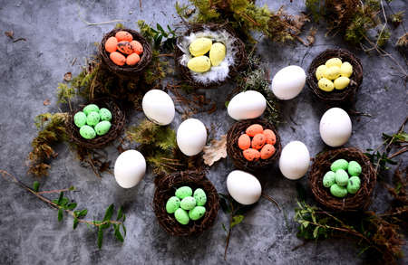 White chicken eggs and bird nests with colored eggs decorated with forest mosses and plants, gray backgroundの写真素材