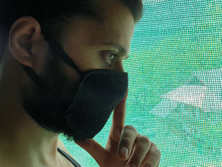 A man is sad, helpless, depressed, in tension thinks on coronavirus.Corona or cover-19 stay home pandemic symptoms deadly virus fever cough covering mouth nose. Model looking outside through green netの写真素材