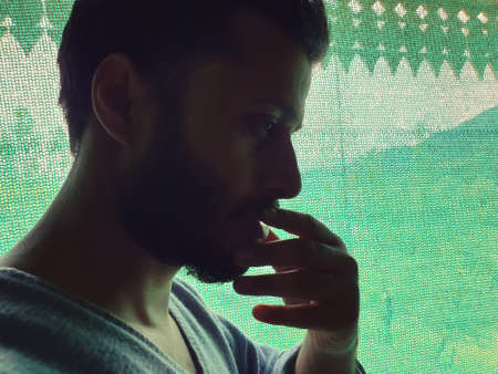 A man is sad, helpless, depressed, in tension thinks on coronavirus.Corona or cover-19 stay home pandemic symptoms deadly virus fever cough covering mouth nose. Model looking outside through green netの写真素材