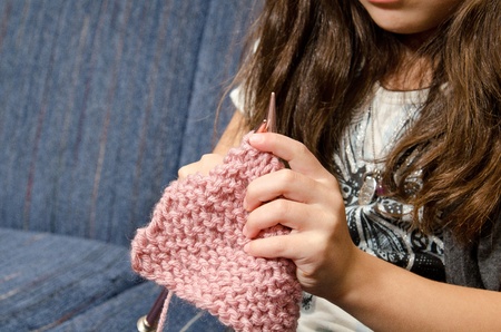 a little girl sits on the couch as she knitts. 