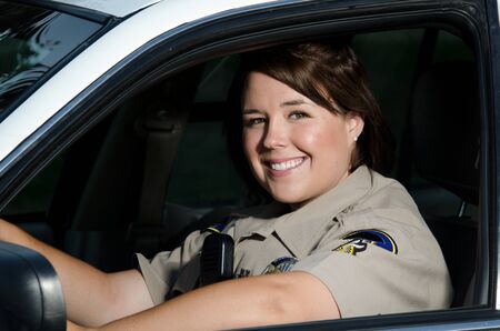 a friendly looking female police officer sits and smiles in her patrol car 